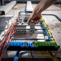 A male electrician works in a switchboard with an electrical connecting cable. Voltage switchboard with circuit breakers are in the ON and OF positions in the big electric box for electrical distribution panel, and temporary electric cables are switched.